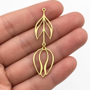 May include: A gold-toned metal jewelry component featuring a vertical design with two openwork leaf or petal shapes connected by a central stem. The top section is a pointed leaf shape, and the bottom section is a rounded, bulbous petal shape.
