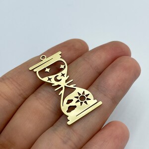 May include: Gold-toned metal hourglass charm with a sun and clouds design on one side and a moon and stars design on the other side.