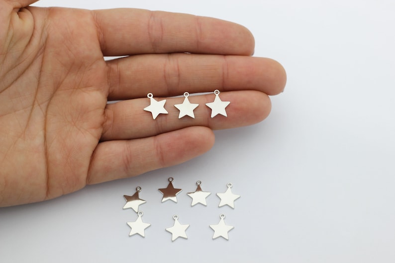 May include: Eight silver star-shaped charms with a loop at the top. The charms are arranged in two rows on a white surface.