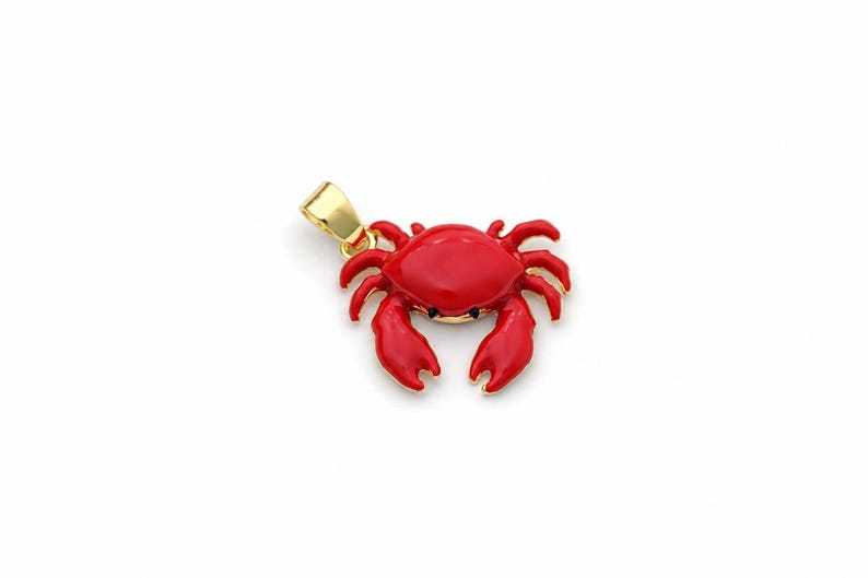 May include: A red crab pendant with a gold-coloured bail. The crab has a detailed design with claws and legs. The pendant is likely made of metal and enamel, and is a nautical-themed jewellery item.