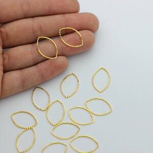 May include: A group of gold-colored metal oval jump rings with a textured surface. The jump rings are scattered on a white surface.