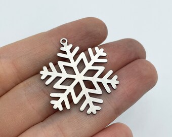 Puede incluir: Un dije de copo de nieve plateado con un bucle en la parte superior para colgar. El copo de nieve es detallado e intrincado, con un acabado cepillado.