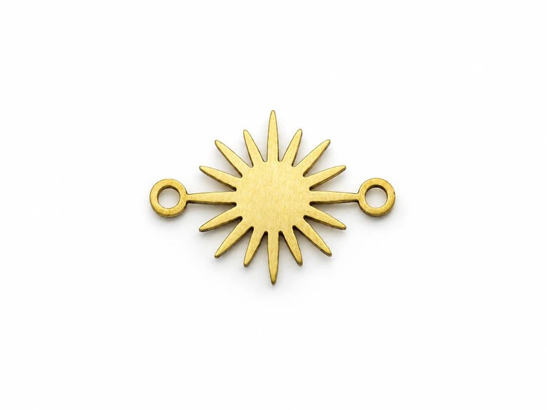 May include: A gold-toned metal jewelry connector featuring a central sunburst design with multiple radiating rays. The component includes a small circular loop on each side, extending horizontally from the sunburst shape for attachment purposes.