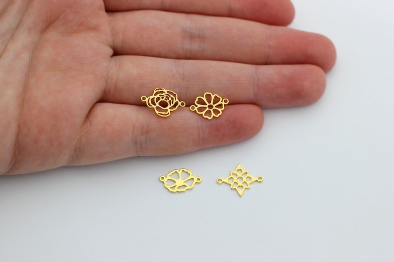 May include: Three gold-toned metal charms in the shape of flowers. The charms have openwork designs and are perfect for jewelry making.