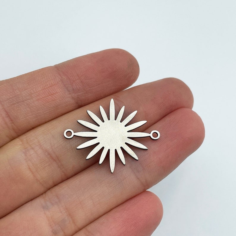 May include: Silver metal charm with a sunburst design and two jump rings. The charm is about 1 inch in diameter.