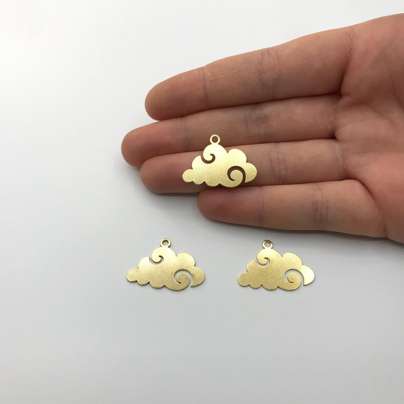May include: Three gold-colored cloud charms with a swirling design. Each charm has a small loop at the top for attaching to jewelry or other crafts. The charms are displayed against a white background.