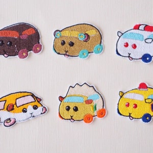 May include: Six embroidered iron-on patches featuring cartoon hamsters driving different vehicles. The hamsters are yellow, brown, and white with black eyes and pink noses. The vehicles include a yellow school bus, a white ambulance, a yellow police car, and a brown, yellow, and blue car.
