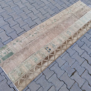 May include: A rectangular, vintage-style rug with a patchwork design. The rug features various neutral tones, including beige, brown, and light green, with geometric and patterned details. The rug is likely made of natural fibers.