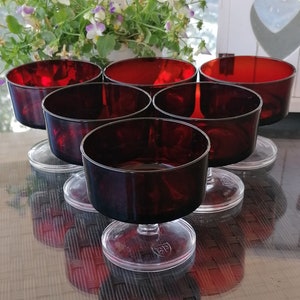 Può includere: Sei coppette da dessert in vetro rosso con basi in plastica trasparente. Le coppette sono disposte in cerchio su una superficie marrone.
