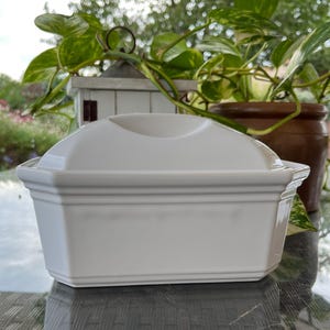 May include: White ceramic rectangular dish with a lid. The dish has a slightly rounded top and a decorative rim.