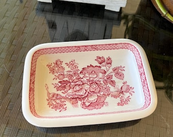 May include: A white rectangular ceramic dish with a pink floral design. The dish has a raised rim and a scalloped edge. The floral design features pink flowers, leaves, and a bird.