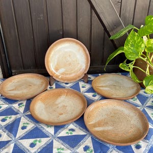 May include: Set of five brown ceramic plates with a white glaze. The plates have a rustic, handmade look and are perfect for serving food.