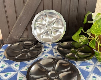 May include: Three silver-colored metal serving dishes with six individual compartments. The dishes are round and have a scalloped edge. The dishes are on a blue and white checkered tablecloth.