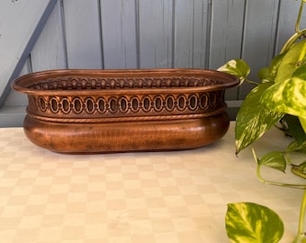 May include: An oval-shaped copper planter featuring a decorative embossed border with a repeating circular pattern along the upper rim. The metal surface displays a warm, burnished finish with subtle variations in tone and a smooth, rounded base.