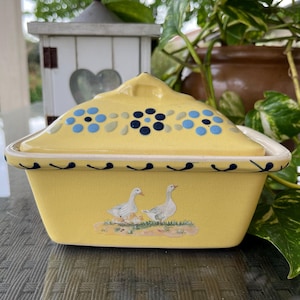 Peut inclure: Un plat à gratin en céramique jaune avec un couvercle. Le plat est décoré de deux oies et de leurs oisons. Le couvercle est décoré d'un motif floral bleu et noir.