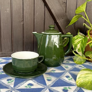 Könnte beinhalten: Eine grüne Teekanne und eine Teetasse aus Keramik mit weißem Innenraum, die auf einer blau-weißen Tischdecke mit Blumenmuster stehen.