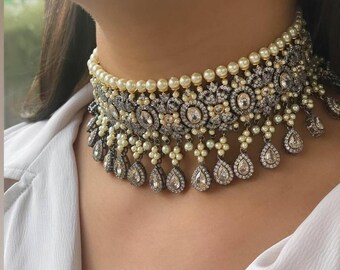 Op de afbeelding: Een zilveren en witte choker ketting met een parel- en diamantontwerp. De ketting heeft een rij parels en een laag ingewikkeld zilverwerk met heldere stenen.