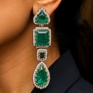 Puede incluir: Elegantes pendientes colgantes con piedras preciosas verdes talla esmeralda en varias formas: un triángulo, un cuadrado, un cuadrado pequeño con una gema azul y una lágrima. Cada gema está rodeada por un halo de pequeños diamantes brillantes.