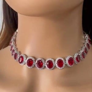 Può includere: Un collier choker argentato con una fila di grandi pietre rotonde rosse circondate da pietre più piccole e trasparenti.