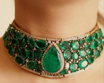 Op de afbeelding: Een luxe choker ketting van smaragd en diamant. De ketting heeft een grote, peervormige smaragd hanger in het midden, omringd door kleinere smaragden en diamanten. De zetting is van goud en de ketting wordt om de nek gedragen.