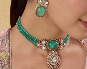 Puede incluir: Un lujoso conjunto de joyas con collar y pendientes a juego. El collar tiene un colgante grande, ovalado, de piedra verde con una gota en forma de lágrima. Los pendientes y el collar están adornados con piedras preciosas transparentes y metal dorado.
