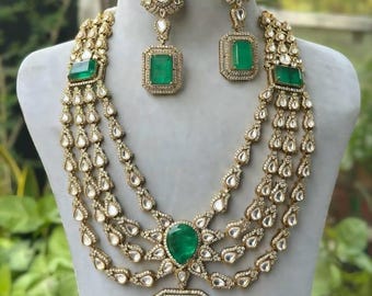 May include: A gold-toned necklace and earring set featuring large emerald-green gemstones. The necklace has multiple strands with teardrop-shaped accents and a large square emerald pendant. The earrings have matching emeralds.