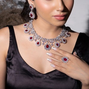 Op de afbeelding: Een vrouw draagt een zwart satijnen topje met een zilveren ketting en bijpassende oorbellen met rode robijnen. Ze draagt ook een zilveren ring met een rode robijn.