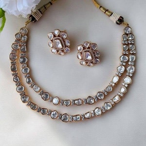 May include: A gold necklace with two rows of clear, faceted stones. The necklace is paired with matching earrings with a similar design.