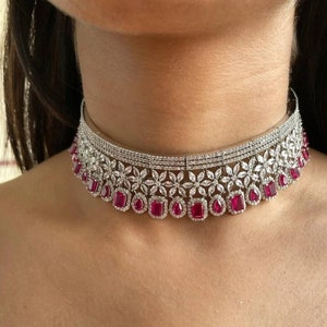 May include: A silver choker necklace with a floral design and red gemstone accents.