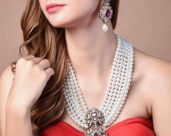 May include: A multi-strand pearl necklace with a large pendant featuring a ruby-colored stone and ornate silver detailing. Matching drop earrings with similar ruby stones and pearl drops complete the set. The jewelry is worn with a red strapless top.