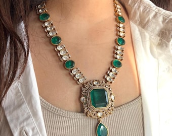 Puede incluir: Un collar de oro con un gran colgante verde esmeralda y piedras verdes esmeralda más pequeñas intercaladas con piedras transparentes.