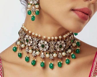 May include: An ornate necklace and earring set featuring emerald green teardrop-shaped stones, white pearls, and clear crystals. The necklace is a choker style, and the earrings dangle. The jewelry is set in a silver-toned metal.