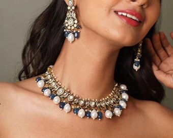 May include: A gold necklace with a delicate design featuring white pearls and blue gemstones. The necklace is accented with intricate details and has a choker style fit.