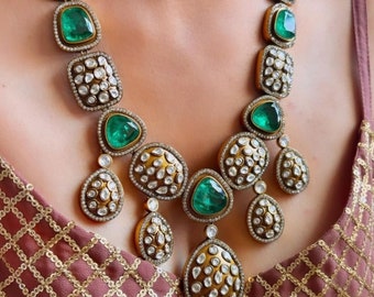 Puede incluir: Un collar de oro con piedras preciosas de color verde esmeralda y transparentes. El collar tiene un diseño en capas con múltiples hileras de piedras.