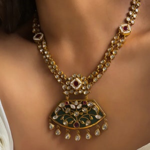 Peut inclure: Un collier en or avec un pendentif vert et blanc orné d'un motif floral. Le pendentif est accentué de pierres rouges et blanches.