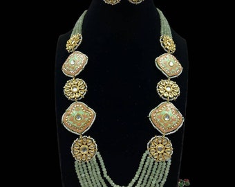 May include: A multi-strand necklace with green beads and gold accents. The necklace features several large, square pendants with intricate designs in shades of pink and green. The necklace is paired with matching earrings.