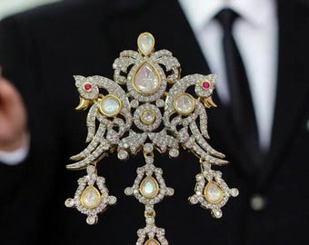 May include: A large, ornate pendant with a gold setting and a central pear-shaped stone surrounded by smaller diamonds. The pendant features a design of two birds with their wings spread, and has three dangling drops with pear-shaped stones.