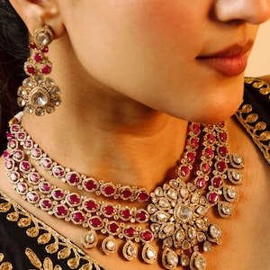 Peut inclure: Un collier en or avec un grand pendentif orné de motifs floraux. Le collier est orné de pierres précieuses rouges et claires.