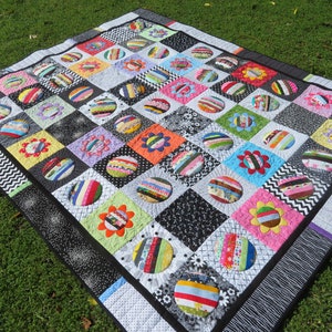 May include: A colorful quilt with a patchwork design featuring black and white squares with circles of various fabrics and colors. The quilt is made with a variety of fabrics, including stripes, polka dots, and floral prints.