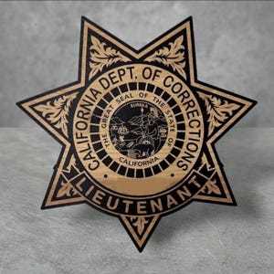May include: A gold and black star-shaped badge with the text "CALIFORNIA DEPT. OF CORRECTIONS" and "LIEUTENANT" around the perimeter. The center of the badge features the Great Seal of the State of California.