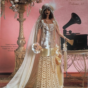 May include: A doll wearing a cream-colored crochet gown with a sequined bodice, a beaded skirt, and a matching flapper hat with a veil. The doll holds a small bouquet and a beaded purse. Text reads Paradise Publications Crochet Collector Costume Volume 77.