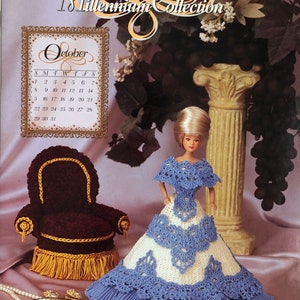 Puede incluir: Una muñeca con un vestido de ganchillo azul y blanco, junto a una silla marrón en miniatura con flecos dorados. La imagen incluye un calendario de octubre y el texto "2000 Millennium Collection."