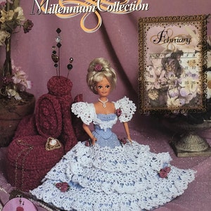 May include: A crochet pattern booklet featuring a doll wearing a blue and white crocheted dress. The doll is sitting on a pink background with a calendar that says "February" and the year 2000. The title of the booklet is "2000 Millennium Collection".