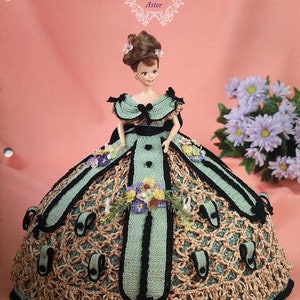 May include: A crochet doll dress pattern for a doll wearing a green and black dress with floral accents. The pattern is titled "Annie's Glorious Gowns Flower Garden Collection Aster".