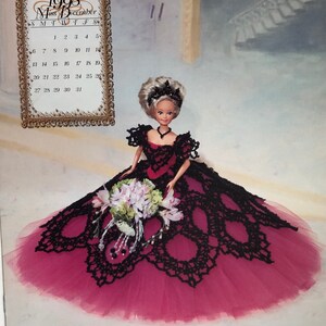 May include: A doll in a black and red gown with a large skirt, holding a bouquet. The doll has blonde hair and a black tiara. A calendar for December 1998 is visible in the background.
