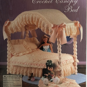 May include: A crochet canopy bed for fashion dolls, in a soft peach color. The bed features a ruffled canopy, bed skirt, and reversible comforter. The image includes the text "Fashion Doll Collector Furniture" and "Crochet Canopy Bed".