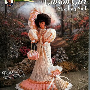 May include: A fashion doll wearing an 1893 Gibson Girl strolling suit, featuring a crocheted cream and peach gown with puffed sleeves, a matching hat with white feathers, a small crocheted handbag, and a miniature parasol with lace trim.