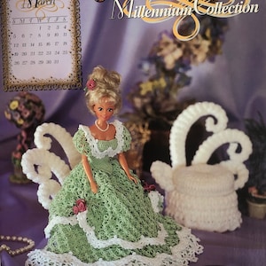 Puede incluir: Una muñeca de crochet que lleva un vestido verde con ribete de encaje blanco y un collar de perlas. La muñeca está sentada en una silla de crochet blanco con un reposapiés de crochet blanco. La imagen incluye el texto "March", "2000 Millennium Collection", y "An Annie Potter Original".