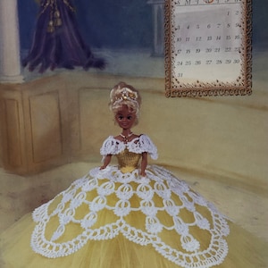 May include: A doll in a yellow and white crocheted gown with a matching bodice and a tiara. The doll is posed in front of a calendar page for May 1998. The image is an Annie Potter original.