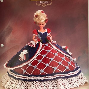May include: A crochet doll dress pattern for a doll wearing a red, white and blue dress with a white lace trim. The pattern is titled "Annie's Glorious Gowns Belle of the Ball Caroline".